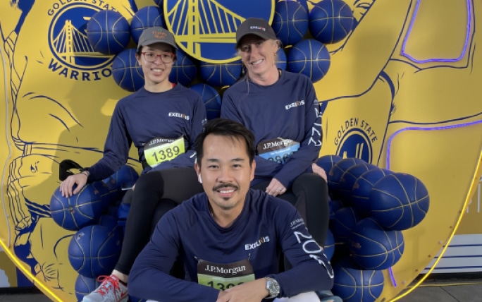 Three Exelixis employees sitting in front of a Golden State Warriors backdrop