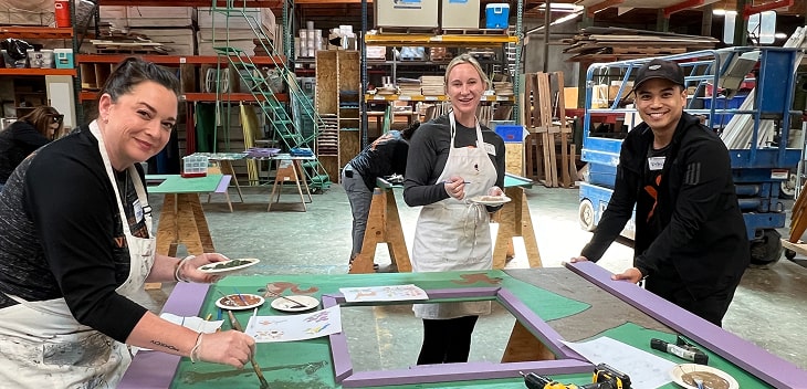 Exelixis employees painting wooden frames at a workshop.