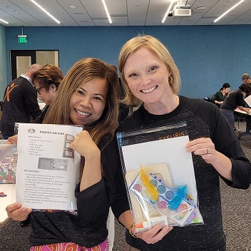 Two smiling employees holding craft kits and instructional sheets.