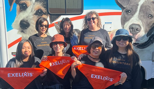 A group of Exelixis volunteers holding orange bandanas in front of a pet adoption vehicle.